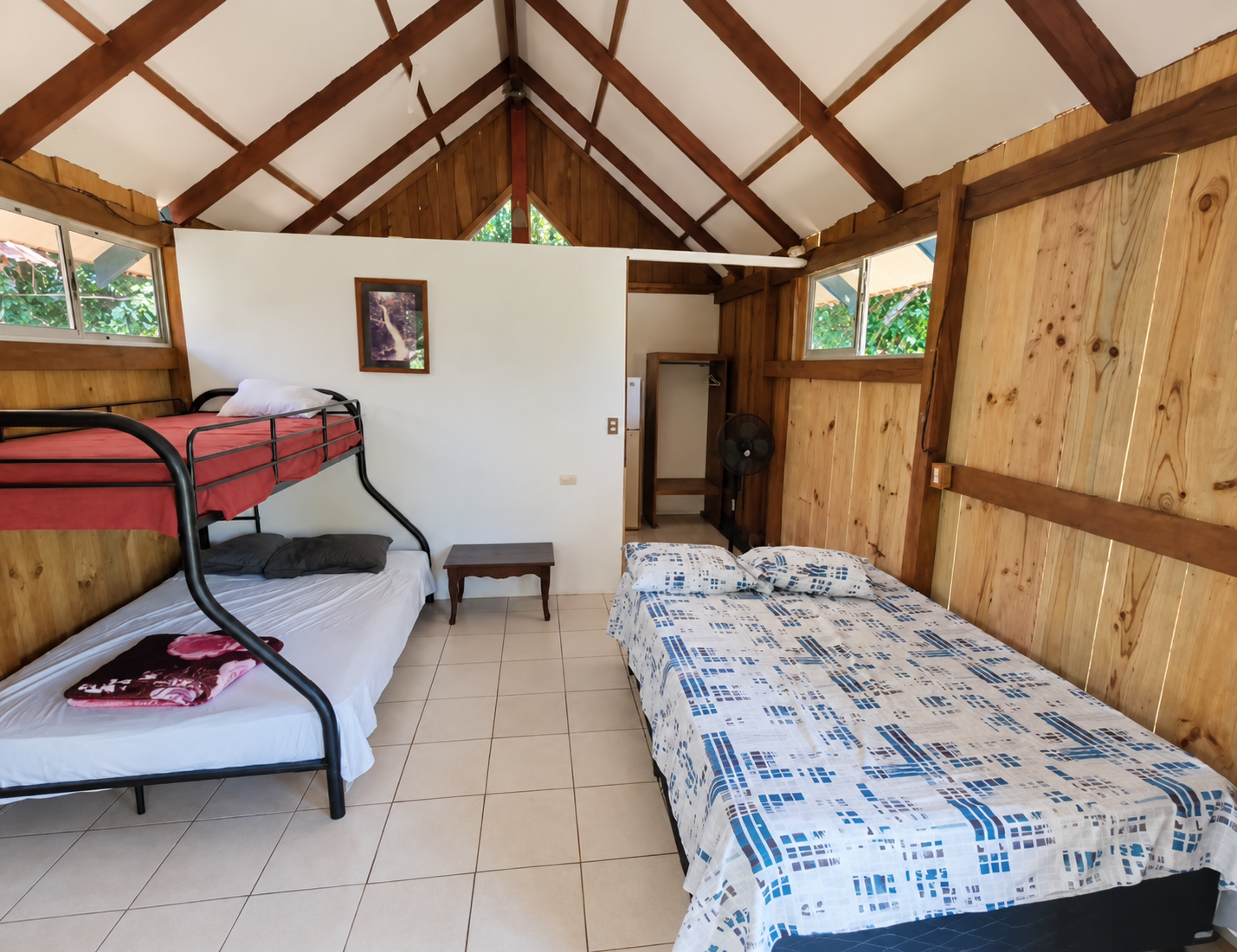 Interior sencillo con cama doble y litera, techo de madera y piso de cerámica